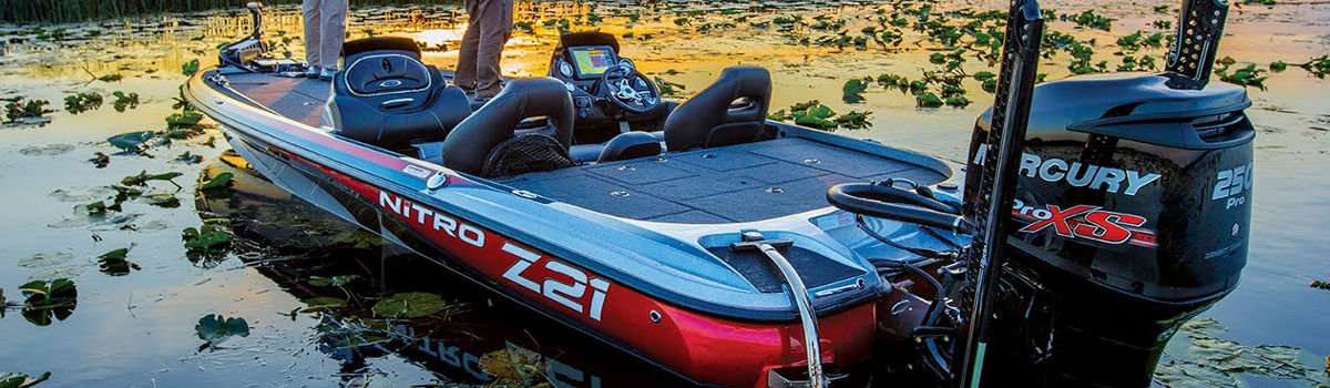 Individual standing at the front of a NITRO boat that's on a lake at sunset.